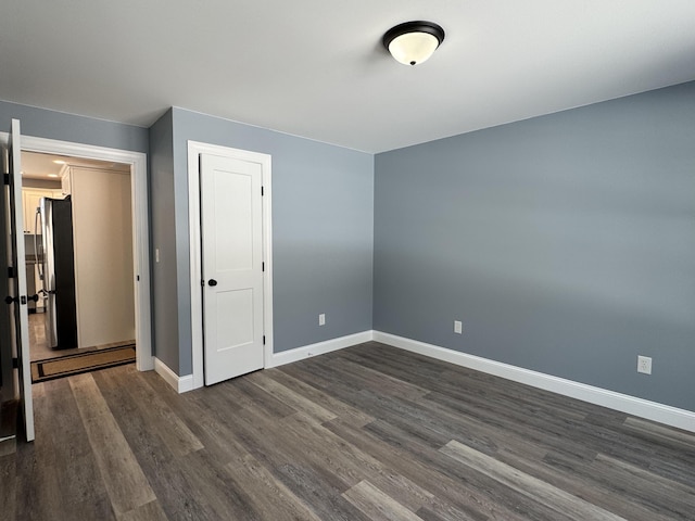 unfurnished bedroom with dark wood-style floors, baseboards, and freestanding refrigerator