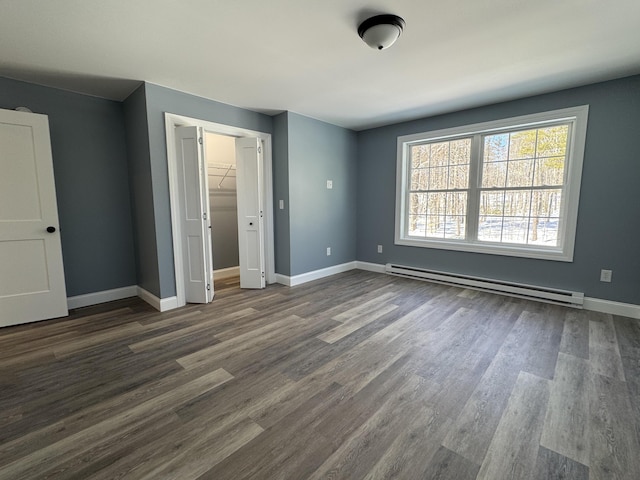 unfurnished bedroom with dark wood-style floors, a walk in closet, a closet, baseboard heating, and baseboards