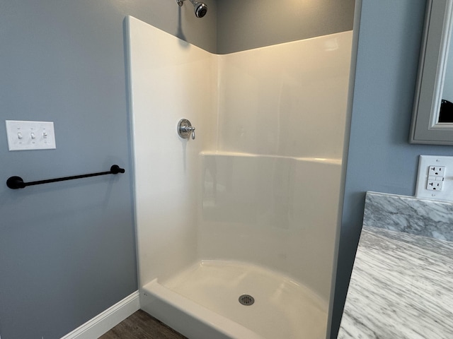 full bathroom with wood finished floors, a shower stall, and baseboards