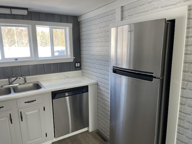 kitchen featuring stainless steel appliances, brick wall, a sink, white cabinets, and light countertops