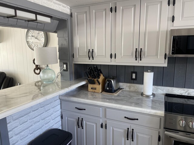 kitchen featuring a peninsula, white cabinetry, stainless steel appliances, and light countertops