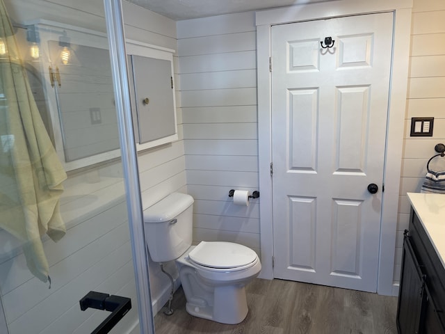 bathroom with toilet, wood walls, wood finished floors, and vanity