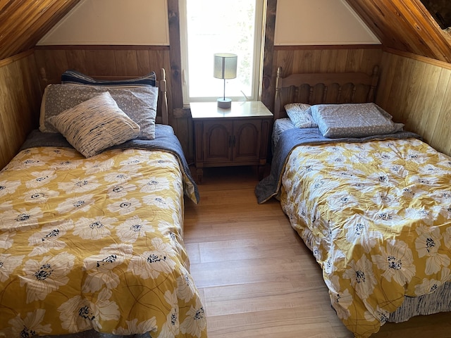 bedroom with light wood-style flooring, lofted ceiling, and wooden walls