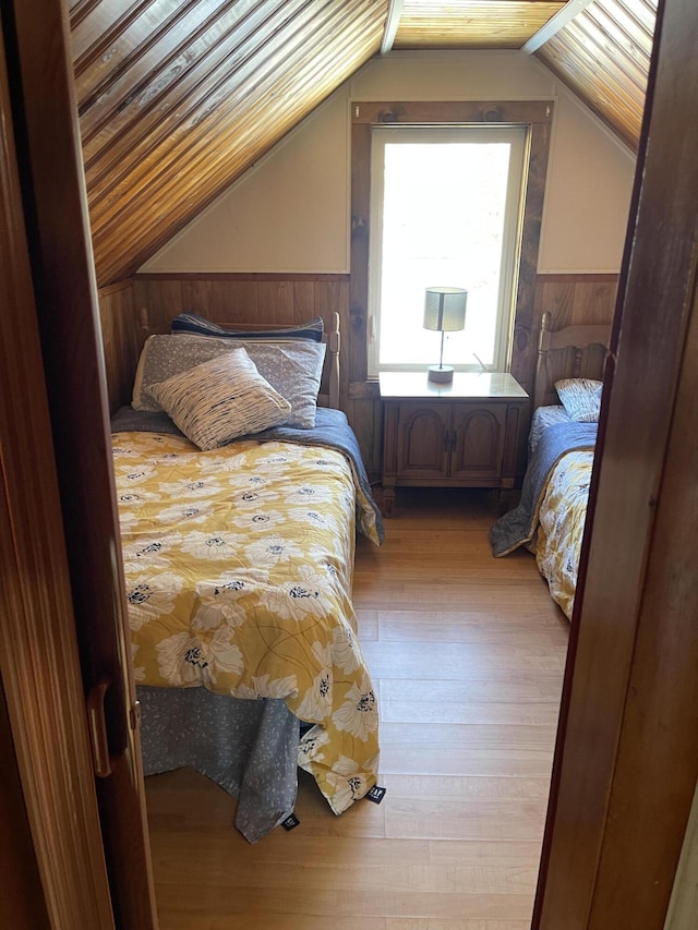 bedroom with lofted ceiling, a wainscoted wall, light wood finished floors, and wood walls