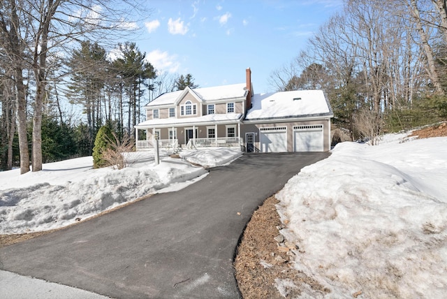 colonial home featuring an attached garage, aphalt driveway, a chimney, and a porch