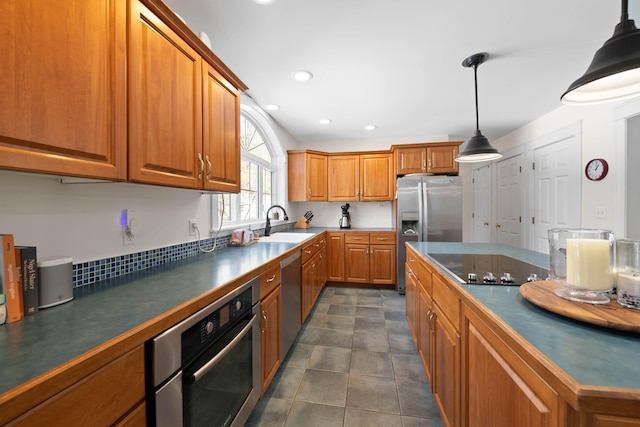 kitchen featuring dark countertops, appliances with stainless steel finishes, brown cabinets, decorative light fixtures, and a sink