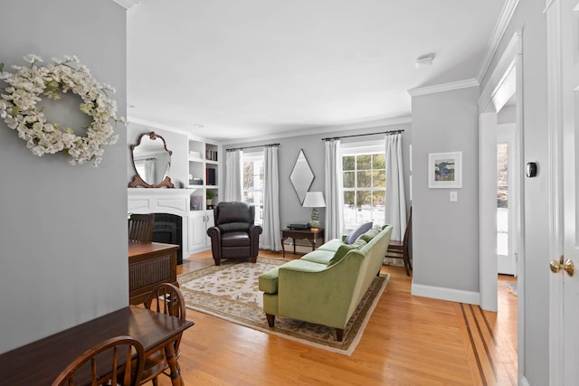 living area featuring baseboards, light wood-type flooring, a fireplace, and crown molding