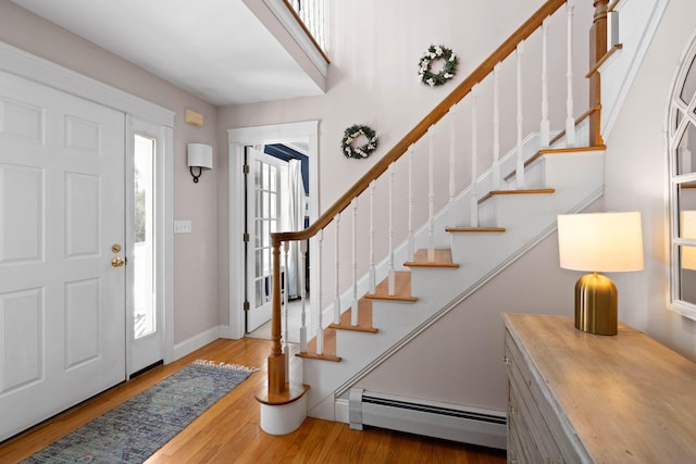 foyer featuring a baseboard heating unit, stairway, wood finished floors, and baseboards