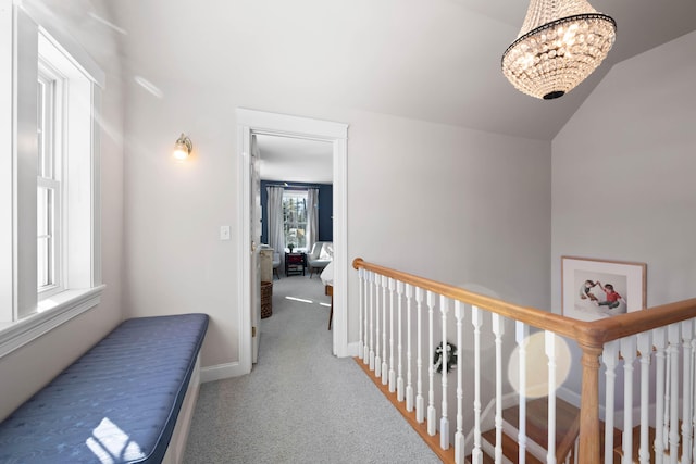 corridor with carpet floors, baseboards, a notable chandelier, and an upstairs landing