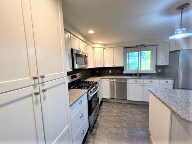 kitchen with hanging light fixtures, light stone countertops, stainless steel appliances, white cabinetry, and a sink