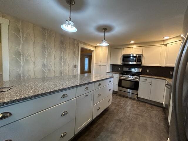 kitchen with stainless steel appliances, stone countertops, white cabinets, and hanging light fixtures