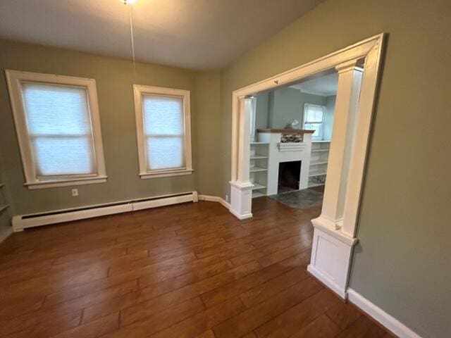 unfurnished dining area featuring dark wood-style floors, decorative columns, a fireplace, and a baseboard heating unit