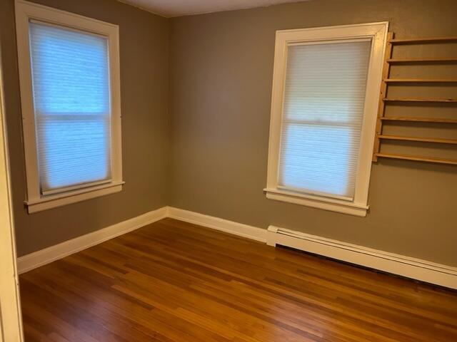 spare room featuring a baseboard heating unit, baseboards, and wood finished floors