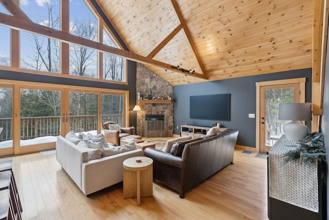 living area featuring beam ceiling, visible vents, light wood-style flooring, wood ceiling, and a stone fireplace