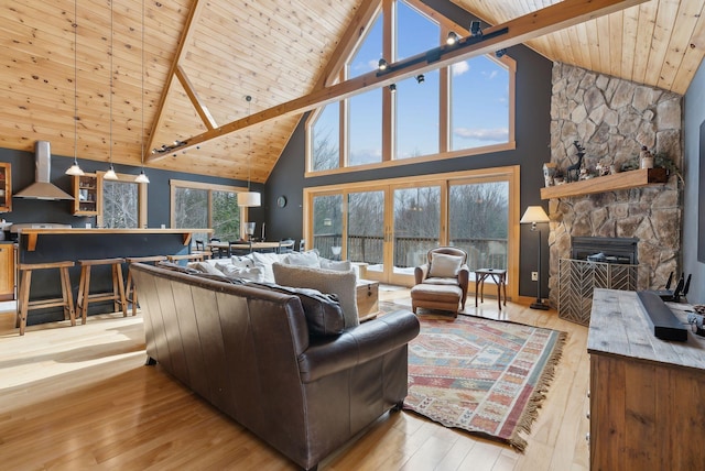 living area featuring vaulted ceiling with beams, wooden ceiling, hardwood / wood-style floors, and a stone fireplace