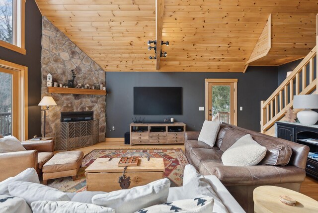 living area featuring a stone fireplace, wood finished floors, high vaulted ceiling, wooden ceiling, and stairs