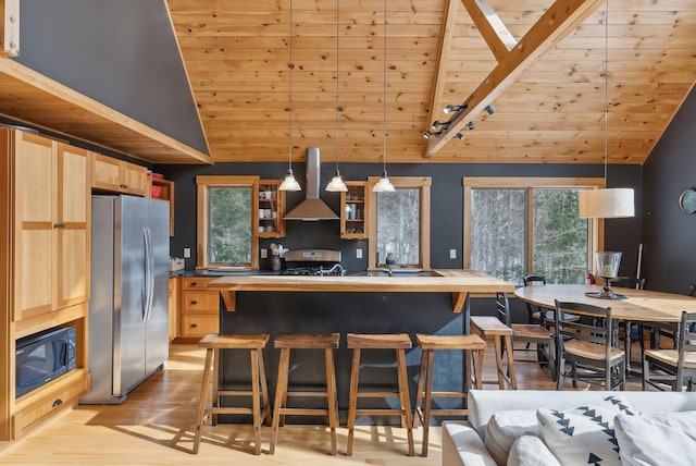 kitchen with black microwave, wood ceiling, range with gas stovetop, wall chimney range hood, and freestanding refrigerator