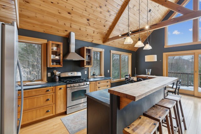 kitchen with vaulted ceiling with beams, appliances with stainless steel finishes, wall chimney range hood, and light wood-style floors