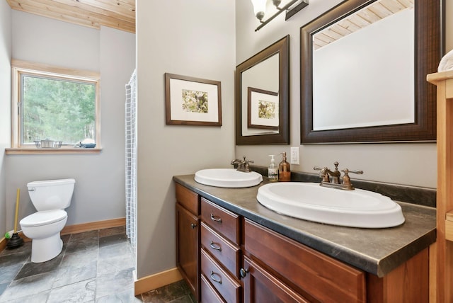 full bath with double vanity, a sink, toilet, and baseboards