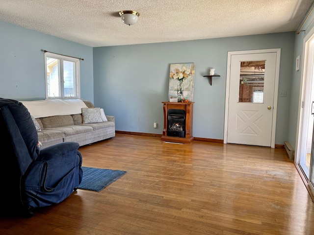 living area featuring baseboards, a lit fireplace, baseboard heating, a textured ceiling, and light wood-type flooring