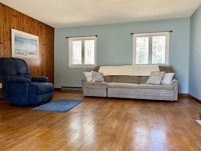 living area featuring a textured ceiling, wooden walls, baseboards, and wood finished floors