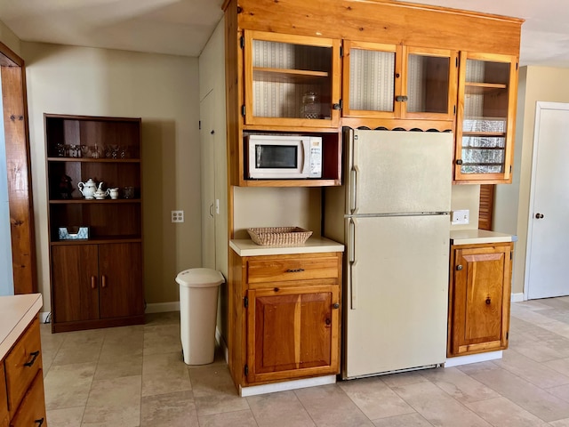 kitchen featuring light countertops, white appliances, and glass insert cabinets