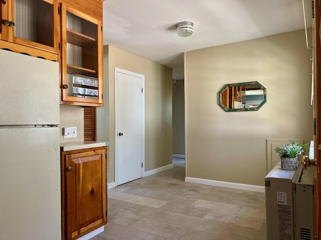 interior space with baseboards, brown cabinetry, glass insert cabinets, freestanding refrigerator, and light countertops