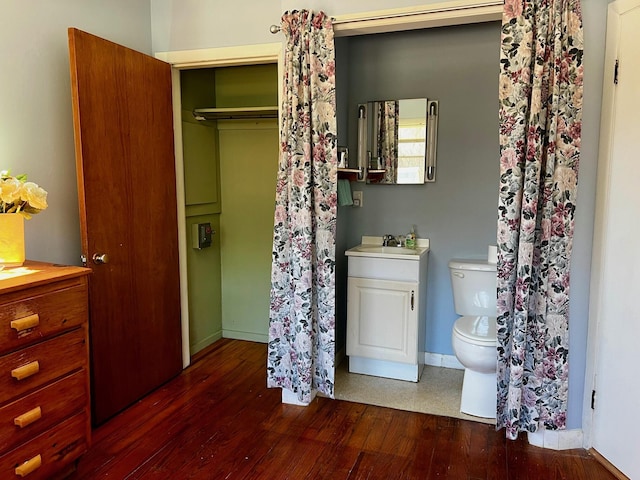 bathroom featuring toilet, a sink, wood finished floors, baseboards, and a closet