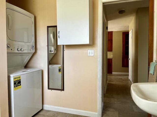 clothes washing area featuring laundry area, stacked washer / dryer, and baseboards