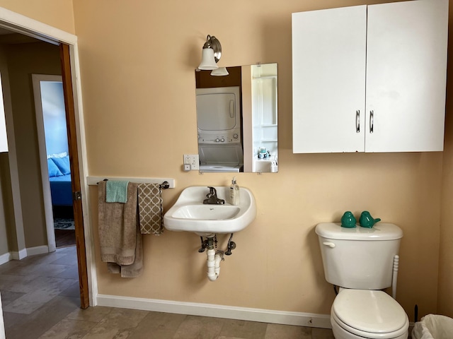 bathroom with toilet, stacked washing maching and dryer, baseboards, and a sink