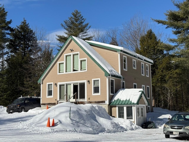 snow covered back of property featuring entry steps, a standing seam roof, and metal roof