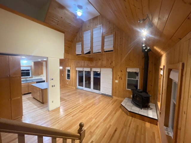 unfurnished living room featuring light wood-style floors, wooden ceiling, wooden walls, and a ceiling fan