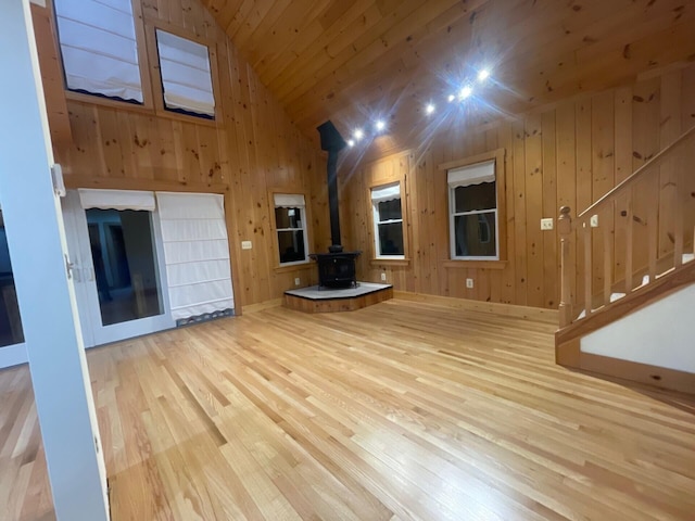 unfurnished living room featuring wooden ceiling, wood finished floors, a wood stove, and wooden walls