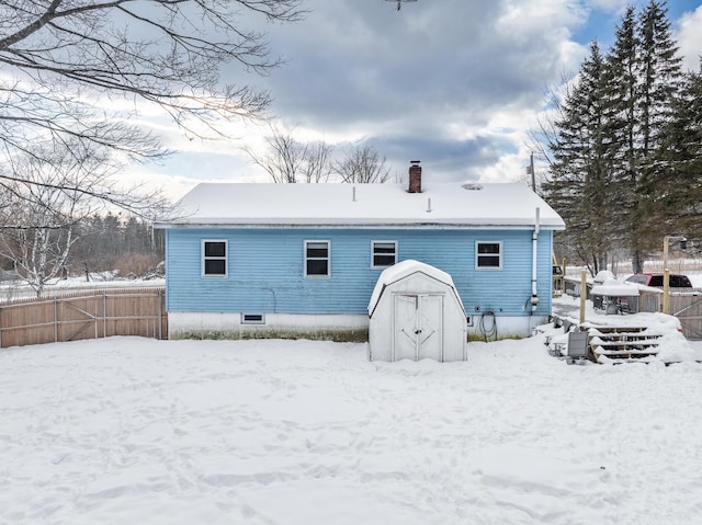 snow covered back of property with an outbuilding, a shed, a chimney, and fence