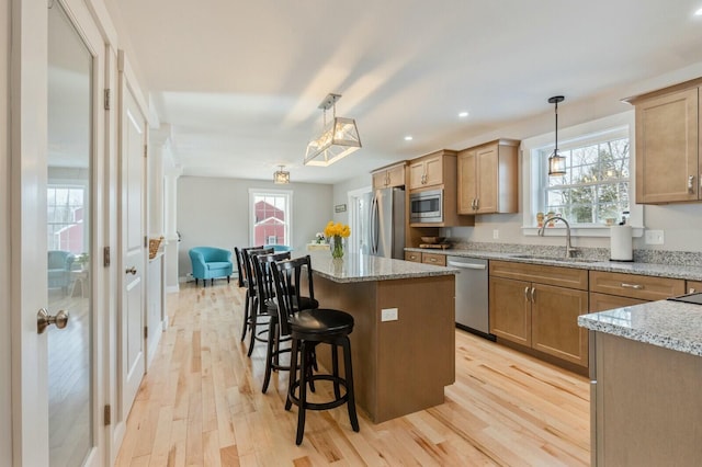 kitchen with stainless steel appliances, a kitchen island, light wood-type flooring, and a sink