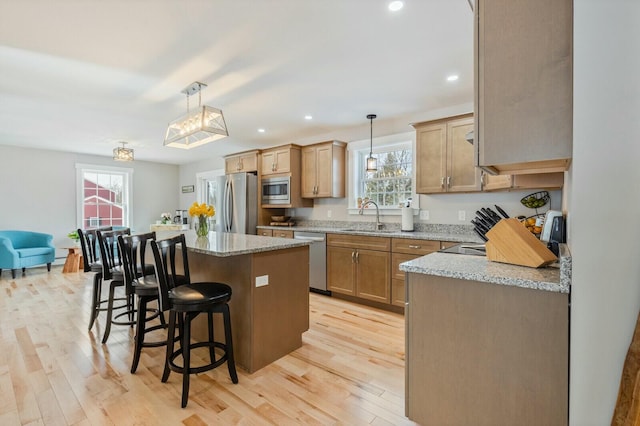 kitchen with light wood-style flooring, a kitchen island, a sink, appliances with stainless steel finishes, and light stone countertops