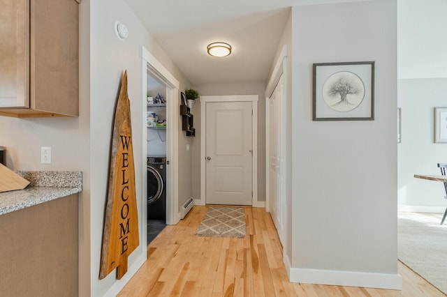 corridor with light wood finished floors, a baseboard radiator, washer / dryer, and baseboards