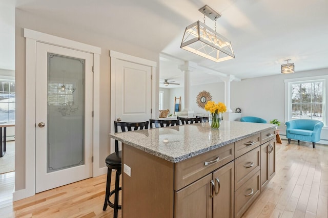 kitchen with light stone counters, light wood finished floors, a breakfast bar area, a kitchen island, and ornate columns