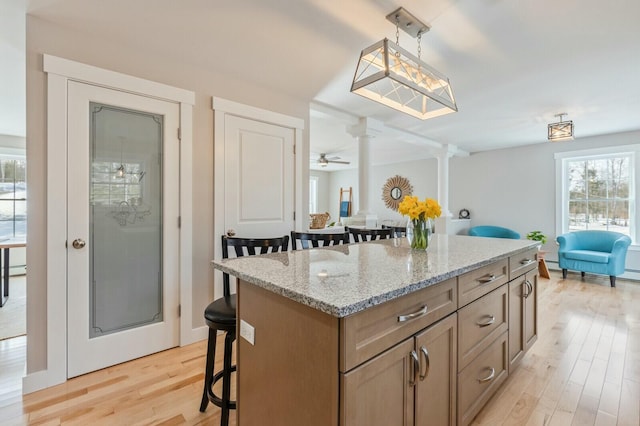 kitchen with light stone countertops, light wood-style floors, decorative columns, and a kitchen breakfast bar