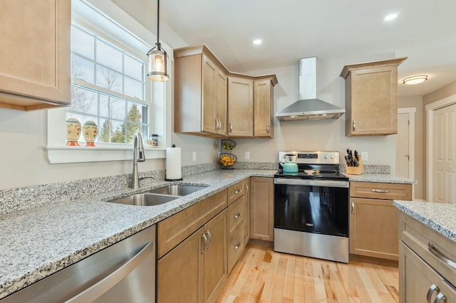 kitchen with light wood finished floors, stainless steel appliances, wall chimney range hood, a sink, and recessed lighting