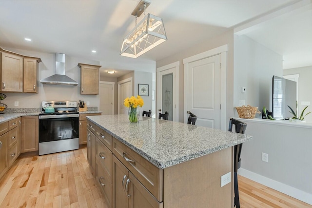 kitchen with light stone counters, a center island, wall chimney exhaust hood, light wood-style floors, and stainless steel electric range