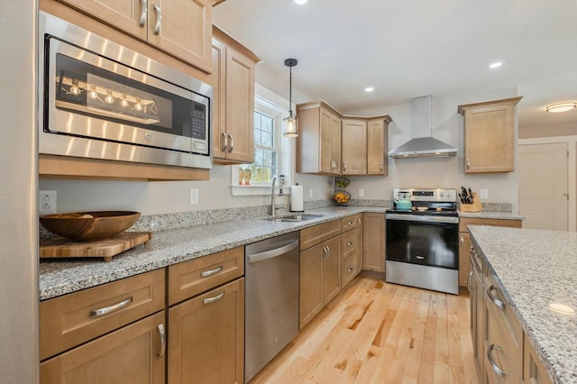 kitchen featuring stainless steel appliances, light wood-type flooring, wall chimney range hood, a sink, and recessed lighting