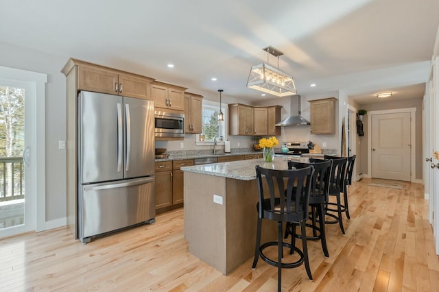 kitchen featuring light stone counters, stainless steel appliances, a kitchen island, wall chimney range hood, and light wood-type flooring