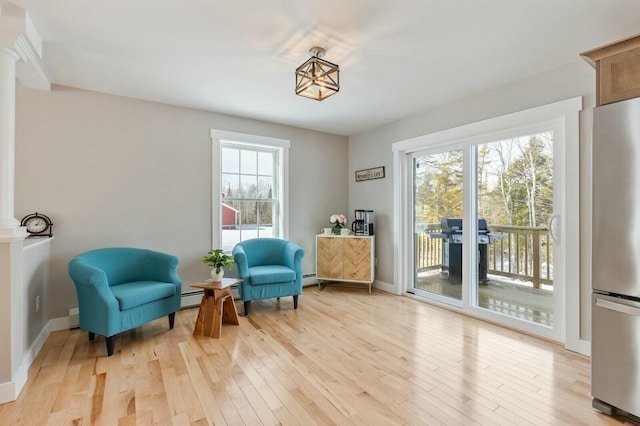 living area featuring a baseboard radiator, a baseboard heating unit, baseboards, light wood-type flooring, and decorative columns