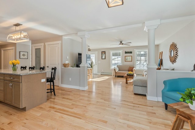 kitchen with open floor plan, a breakfast bar area, light wood-style flooring, and ornate columns