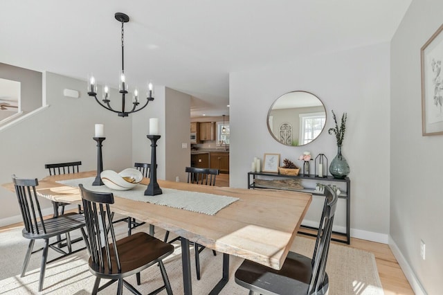 dining space featuring light wood-style flooring, baseboards, and a notable chandelier