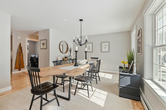 dining area featuring a notable chandelier, a baseboard radiator, light wood-style flooring, separate washer and dryer, and baseboards