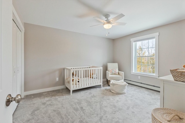 carpeted bedroom with a closet, baseboard heating, a ceiling fan, a crib, and baseboards