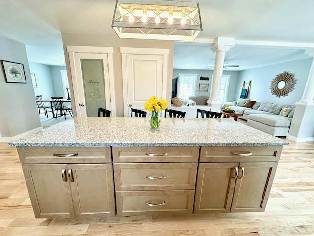 kitchen with light wood-type flooring, decorative columns, and light stone countertops