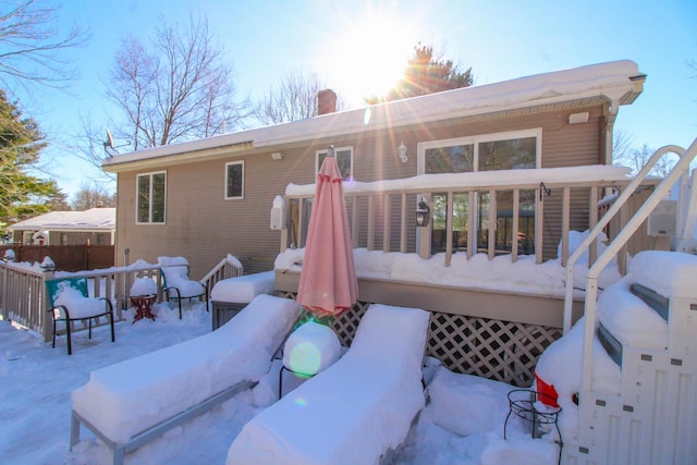 snow covered back of property with a deck and a chimney